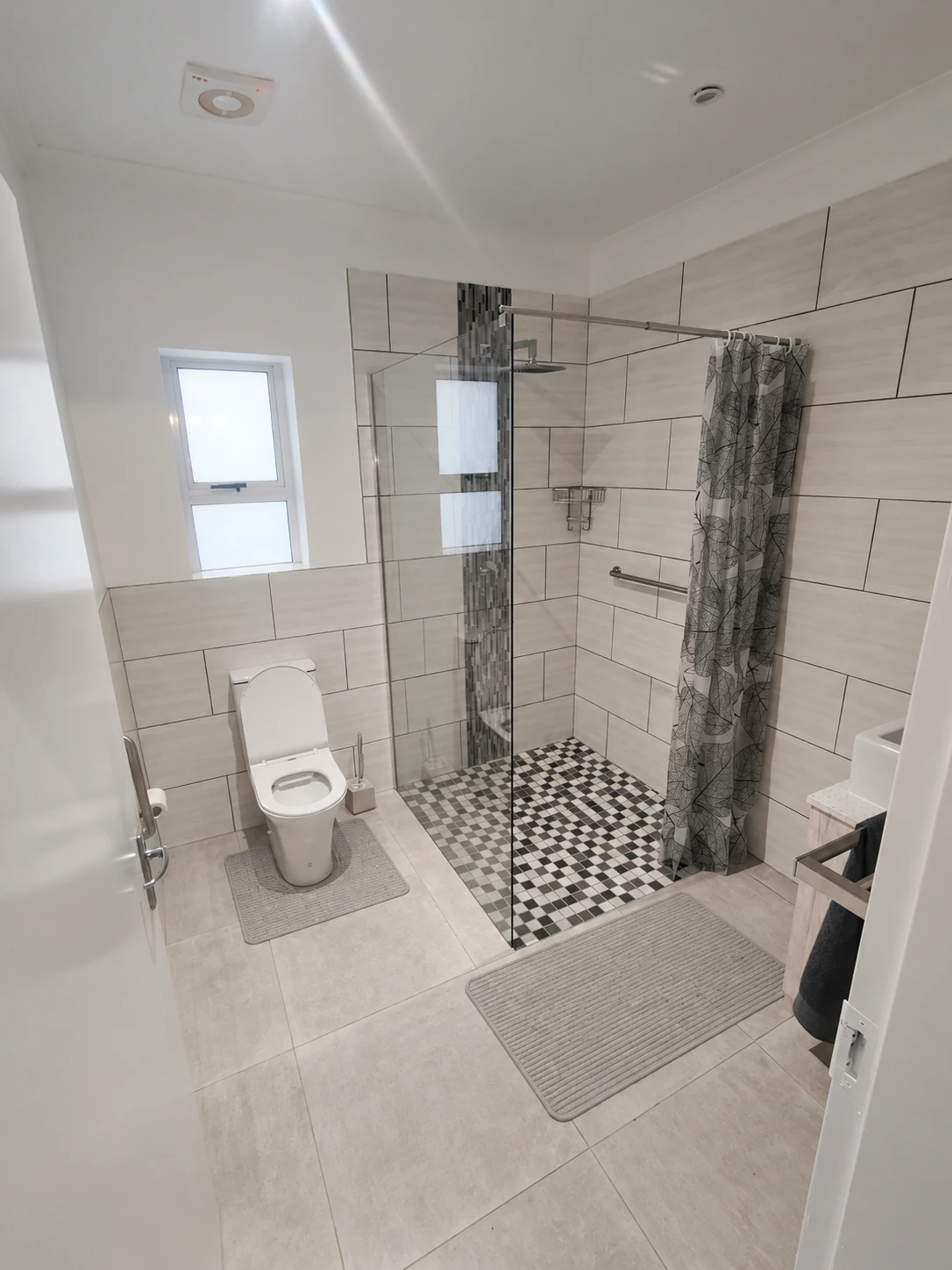 Bathroom overview with toilet and shower; two floor mats digitally added and blue bottle removed
